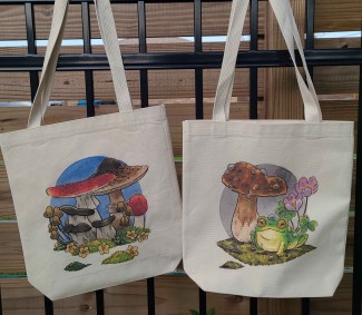 Mushroom tote bag and frog and mushroom tote bag hanging from a fence